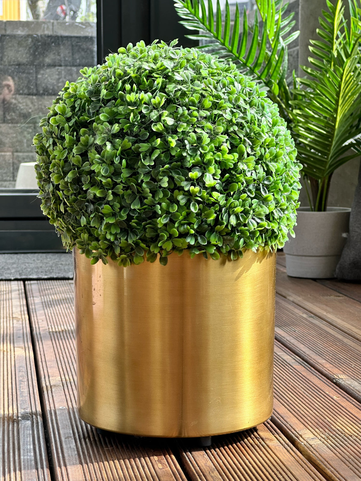 Gold-coloured plant pot raised on Potteben feet on a wooden terrace